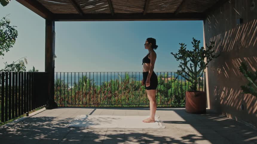 Woman stands on a yoga mat on the porch of a house on a summer day