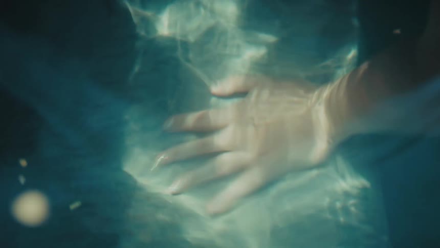 Closeup of a hand gently resting a rock in rippling water with soft abstract light patterns