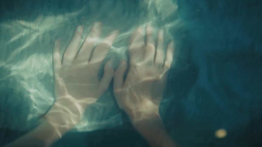 Human female hands submerged in water with sunlight shining on them outdoors during day time
