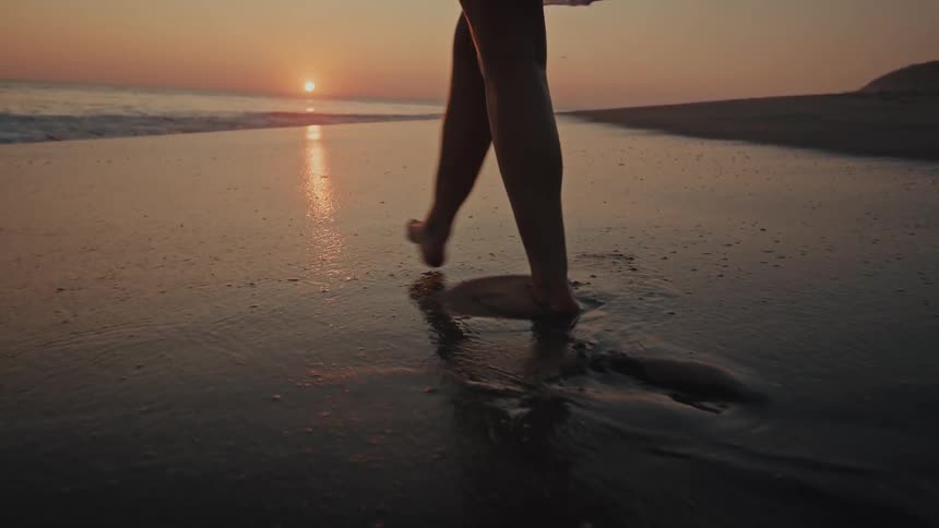 A woman walking down a beach at sunset