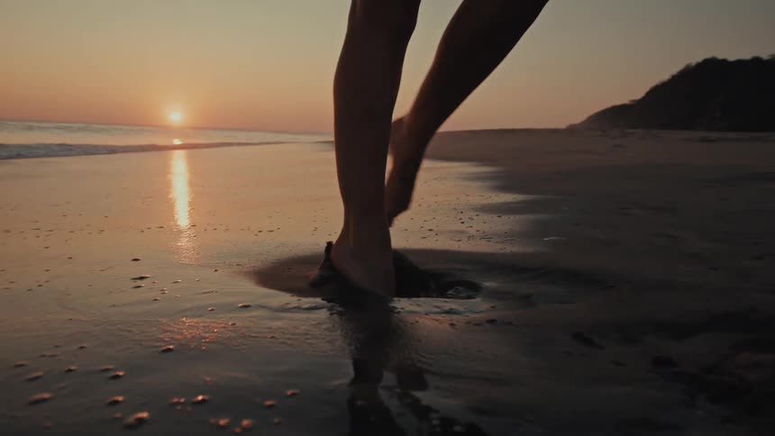 A woman playfully twirls barefoot along the shoreline at sunset