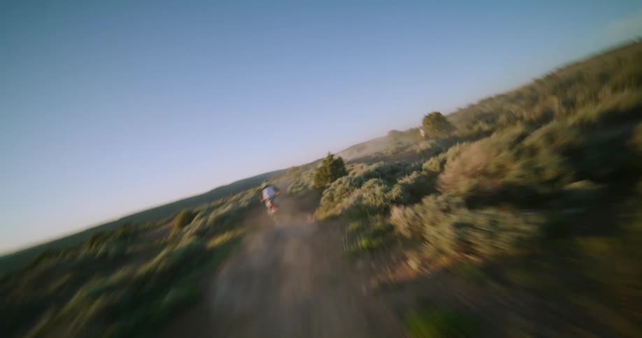 A drone captures a highspeed chase of a rider on a dirt bike as they kick up thick dust while navigating a winding offroad trail through a vast desert landscape during the warm glow of sunset