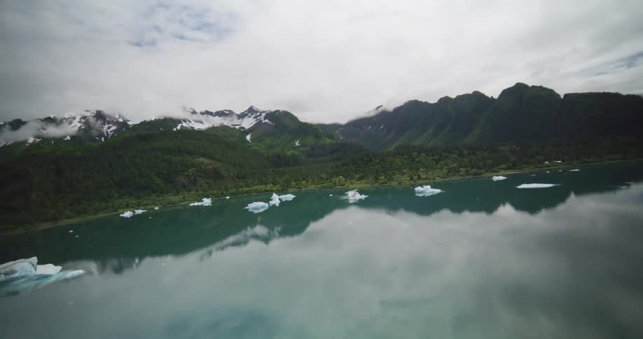 Calm lake with floating ice blocks in front of mountains covered by vegetation and snow