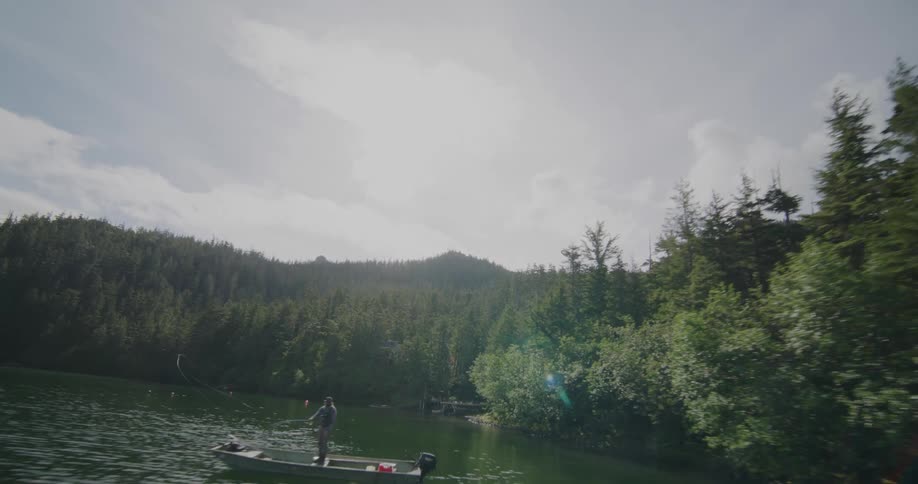 Person fishing from a small boat on a lake surrounded by forest