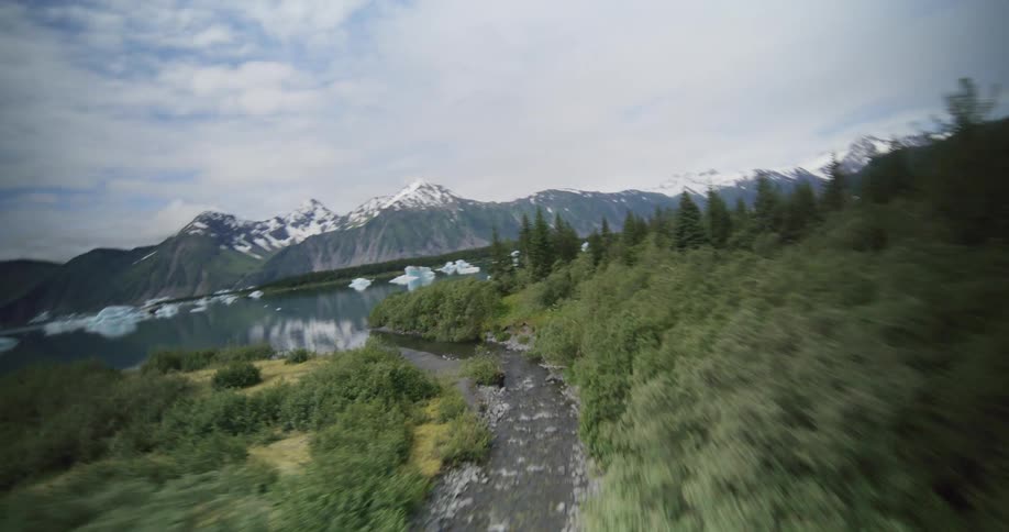 Aerial view of a winding river flowing through forest toward icy mountains and a glacier lake