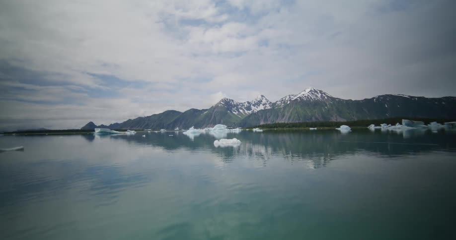Calm lake with floating ice blocks reflecting snowcovered mountains in the background