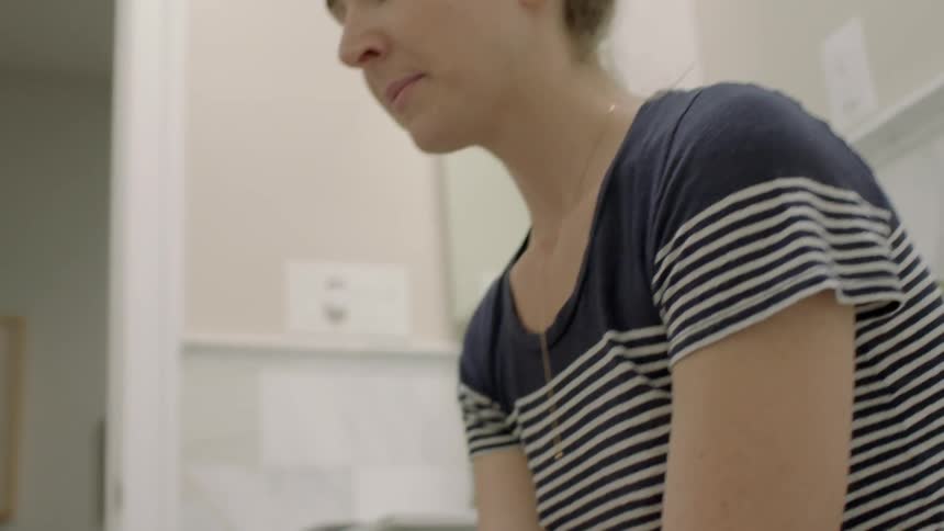 Woman sitting in bathroom and staring down at pregnancy stick in hand