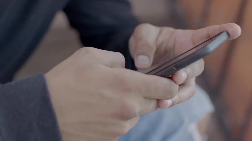 A man is using both thumbs to operate his phone