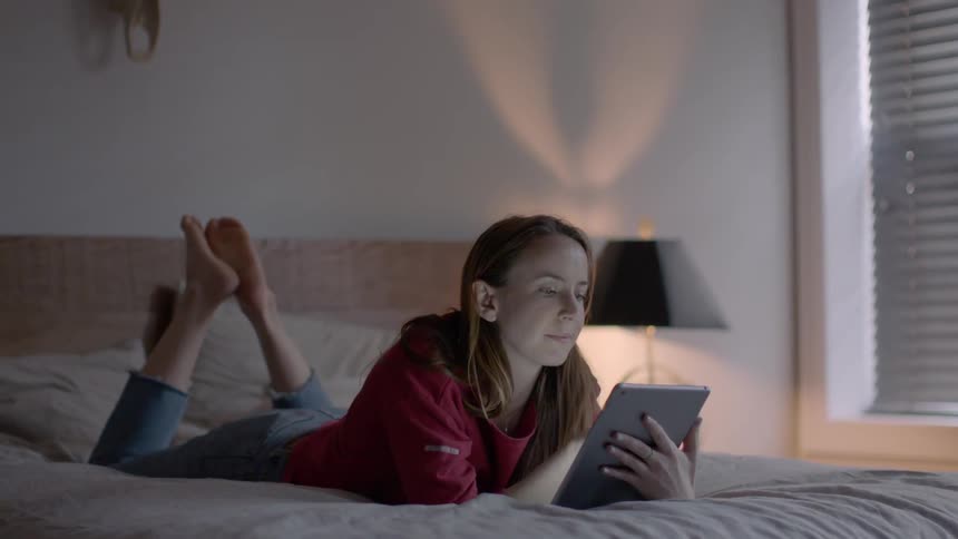 A woman is laying in bed using a tablet