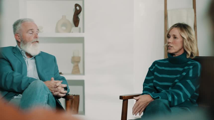 Couple seated in armchairs talking in a naturally lit indoor setting
