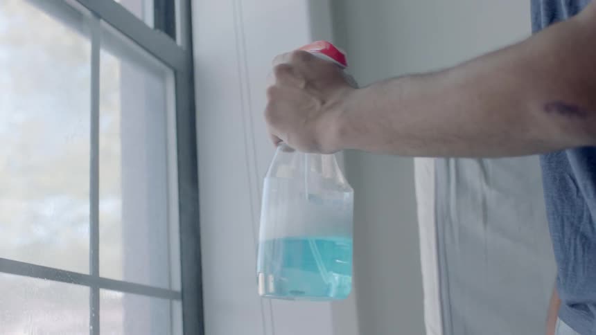 Person squirting a window with cleaner and then wiping it down