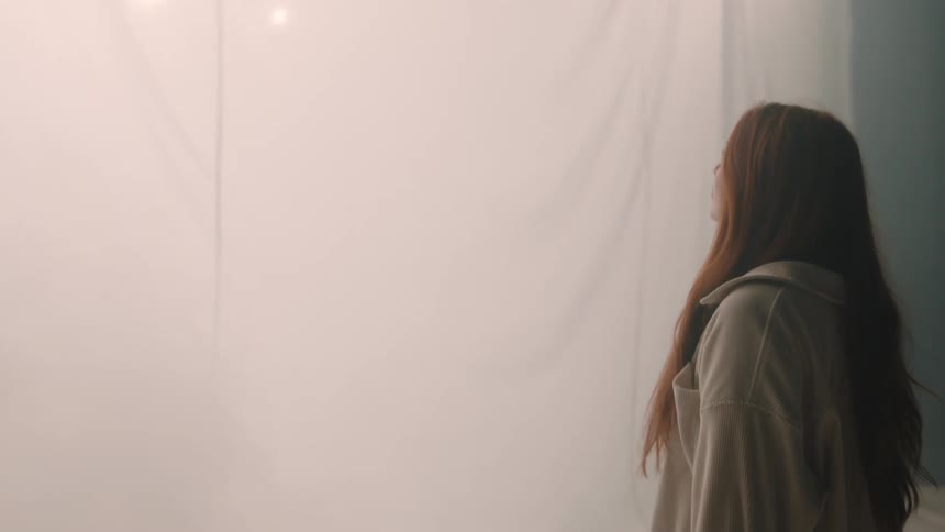 Woman observing a white curtain in a spacious environment with diffused light