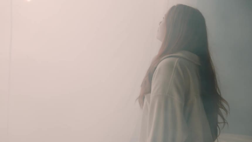 A young woman with long red hair walks through a large tent filled with white smoke moving toward a bright light ahead
