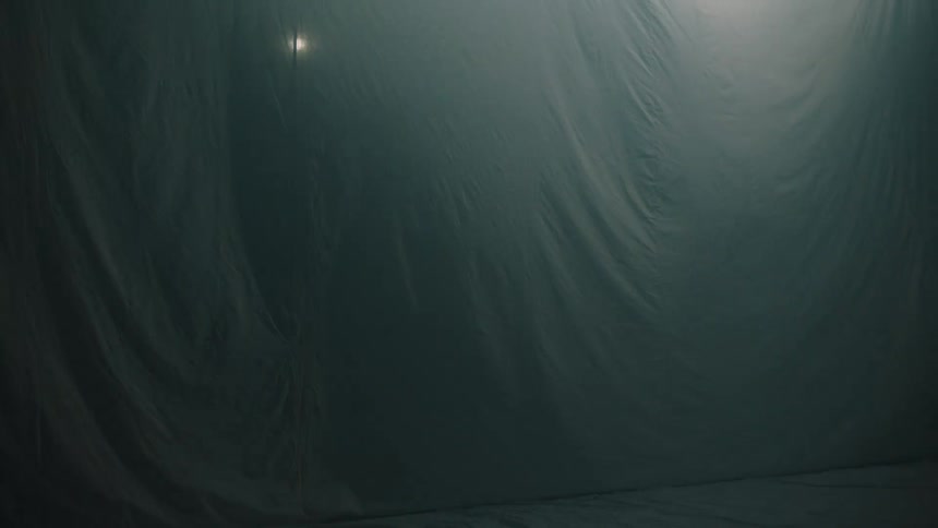 A greenlinen tent ripples in the wind at night its fabric shifting gently as flickering light glows from within