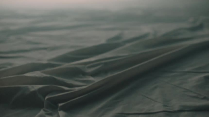 A dark wrinkled fabric or plastic sheet covers a flat surface fog or mist hangs low over the textured material in a dimly lit setting