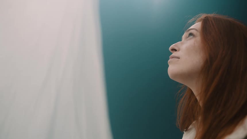Woman standing in front of a blue wall gazes up toward the top of hanging white fabric