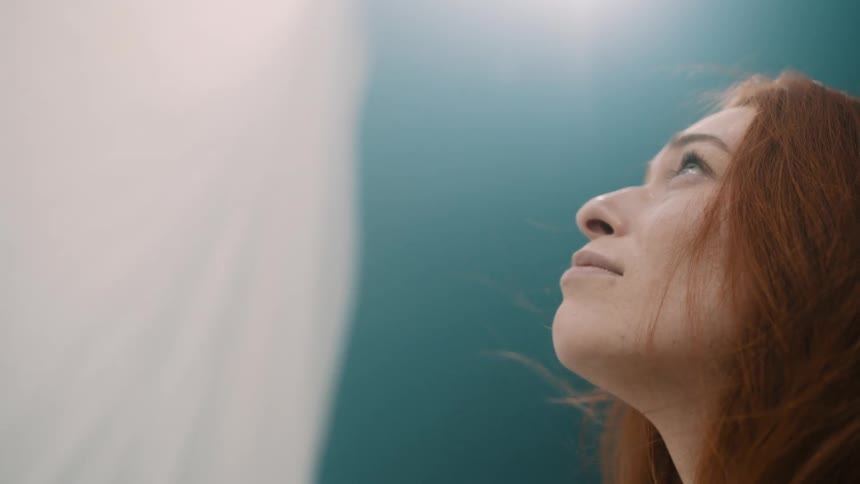 Redhead woman looking at a white curtain with a contemplative facial expression indoors