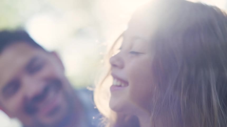 Father and daughter blows on a dandelion while smiling outdoor at dawn