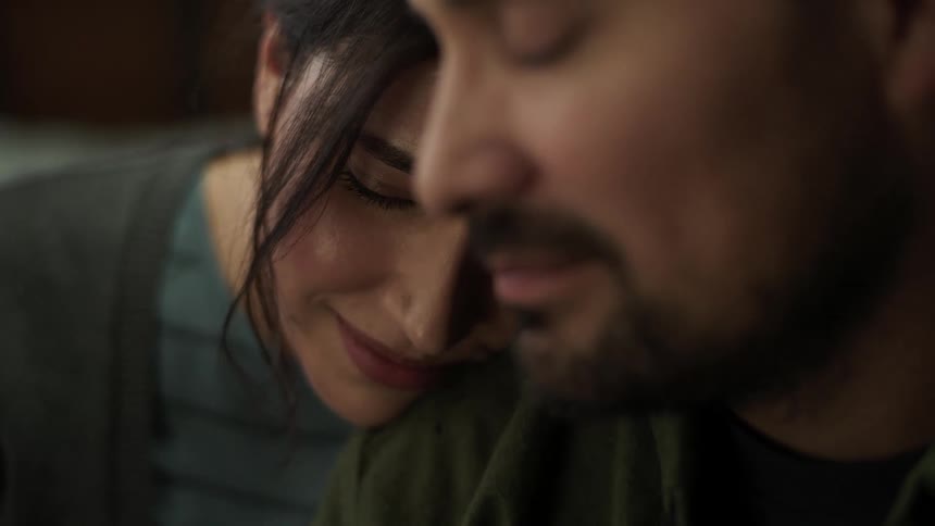 A couple smiles warmly at each other as the young woman rests her head gently on the mans shoulder