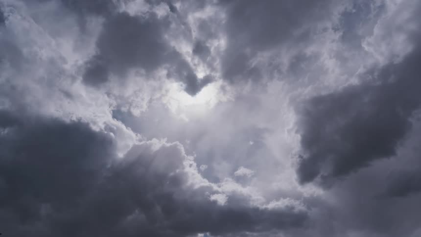 Dramatic dark storm clouds drift slowly across the sky partially obscuring the sun whose brilliant rays pierce through the gaps in a breathtaking and moody display of light