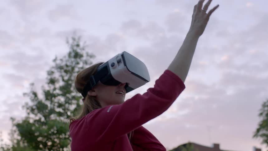 A woman is using vr headset outside at sunset