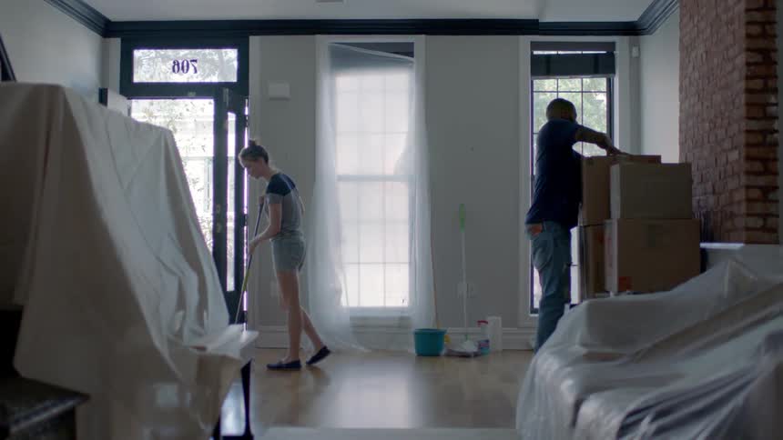 A woman sweeps while a man unpacks boxes