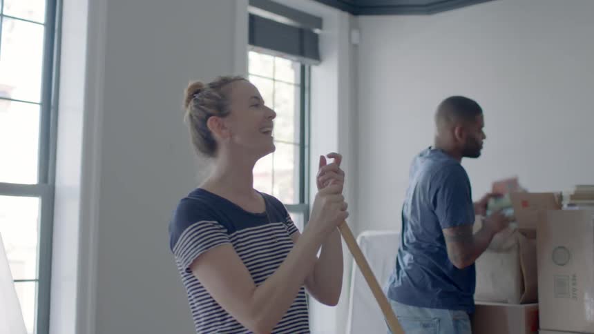 A woman sweeps while a man unpacks boxes