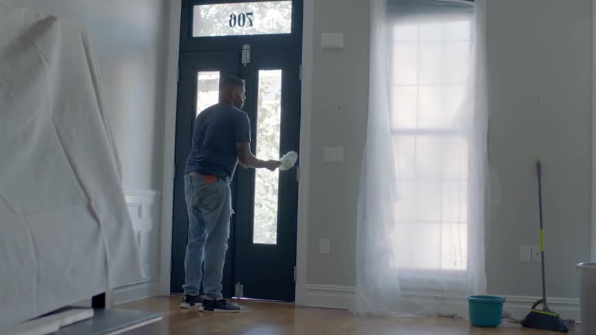 A man uses a feather duster on a door