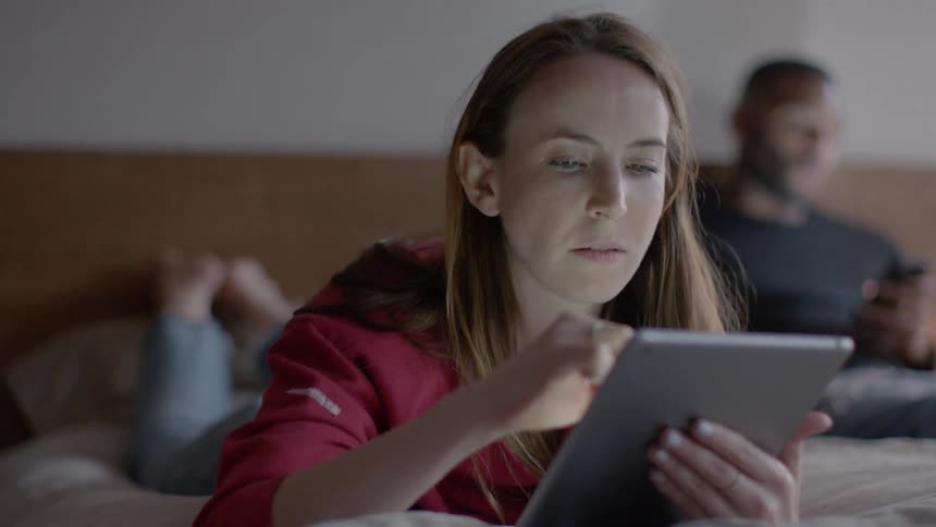 A woman uses a tablet while sitting on a bed