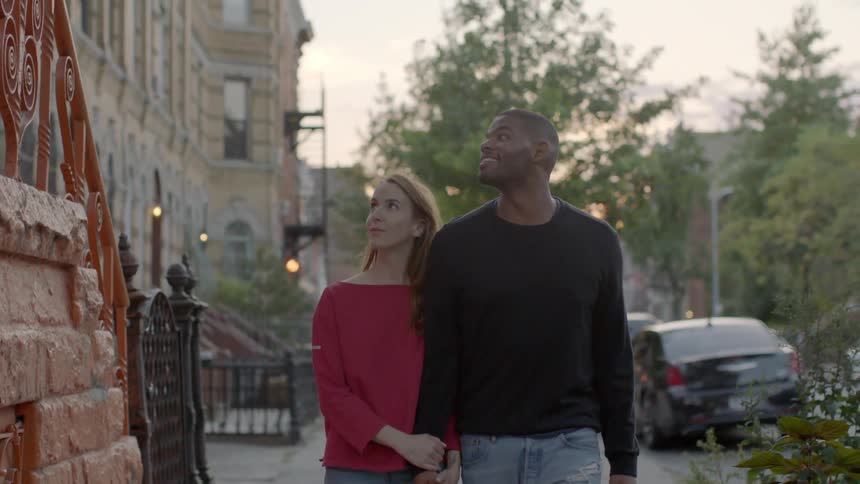 A man and woman hold hands while walking on a city sidewalk