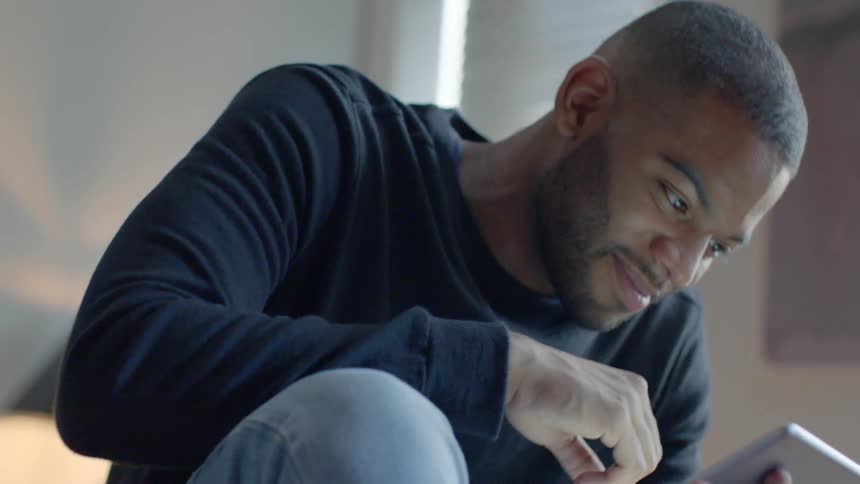 A man smiles while using a tablet