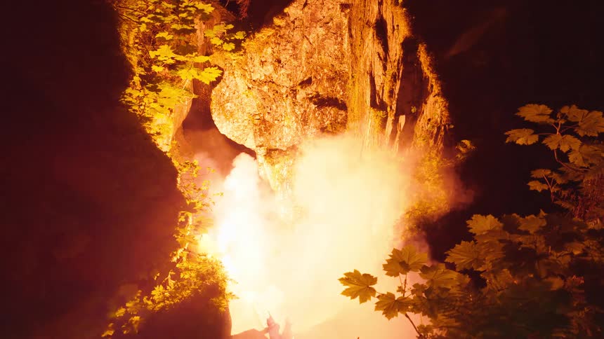 Bright explosion among rocks and foliage in a nighttime setting