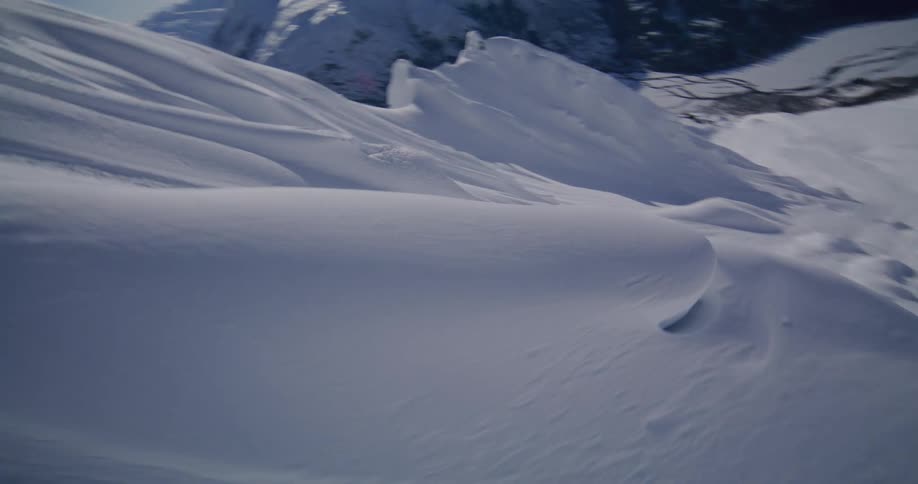 A thrilling highspeed aerial shot dives and swoops down a vast snowcovered mountain skimming over sharp ridges and pristine powder under a clear blue sky