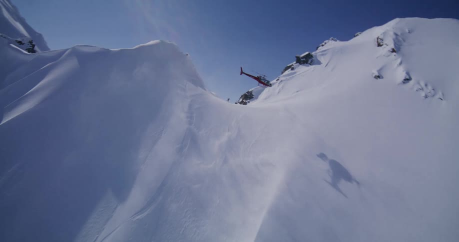 A helicopter flies over arctic mountains in winter the rugged peaks completely covered in snow under the bright midday light