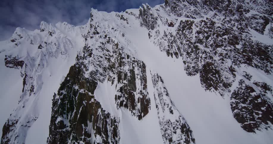 Snowcovered mountain slopes with exposed rock under a partly cloudy sky
