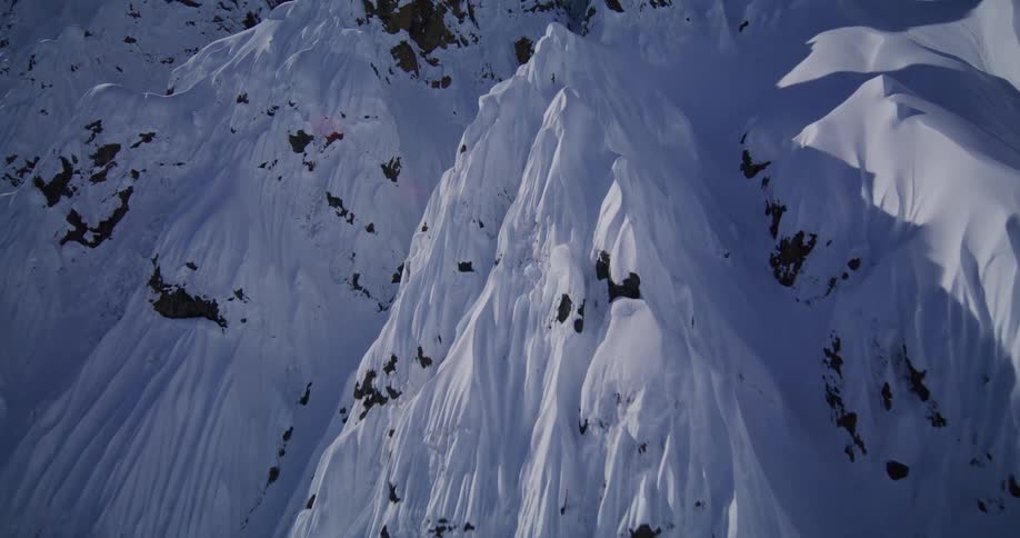 An expert skier carves a perilous path down the razorthin edge of a steep snowcovered mountain ridge captured from a breathtaking aerial perspective