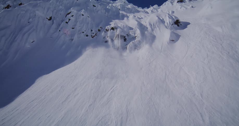 Snow slide creates a powder cloud on a steep icecovered mountain slope