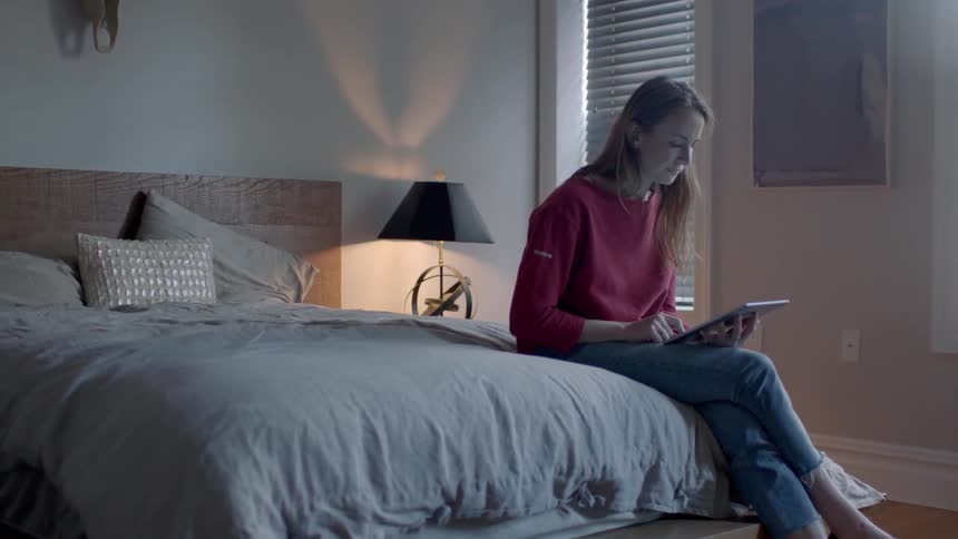 A woman uses a tablet while sitting on a bed