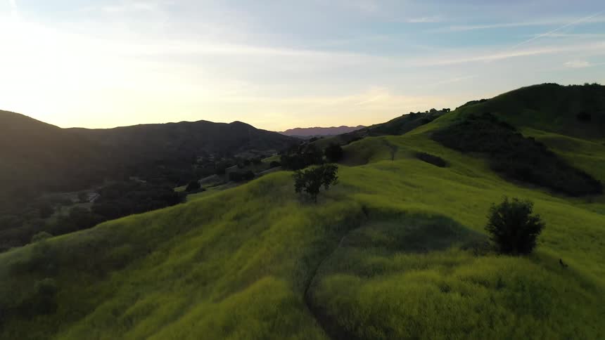 Winding path through green hills at sunset with mountains in the background