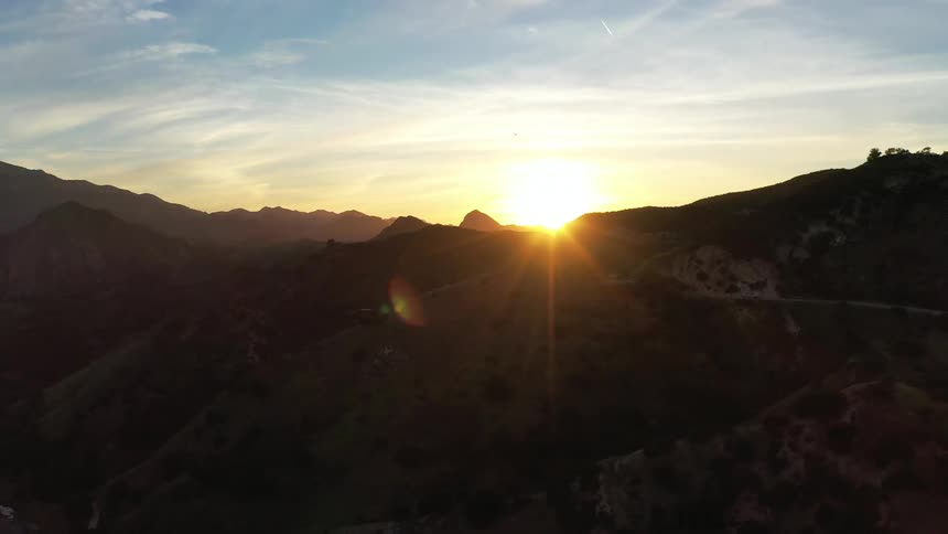 Sun setting behind a mountain range under a partly clear sky