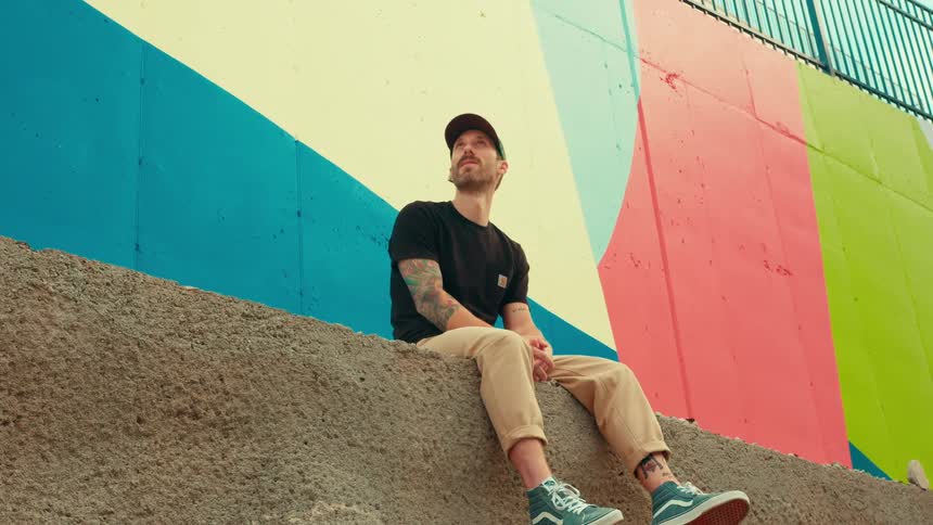 Person sitting on a wall in front of a colorful geometric mural in an urban area