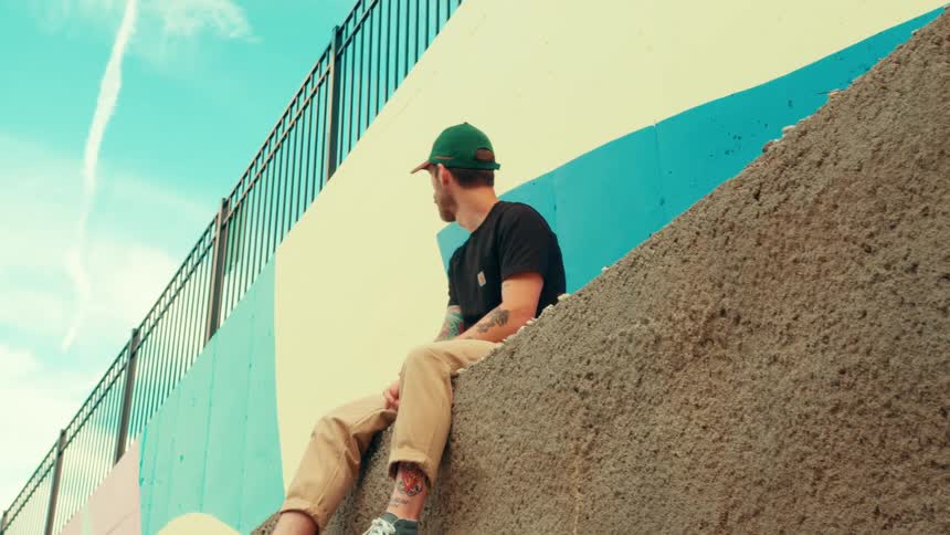 Person sitting on a sloped wall in front of a geometric mural under a blue sky