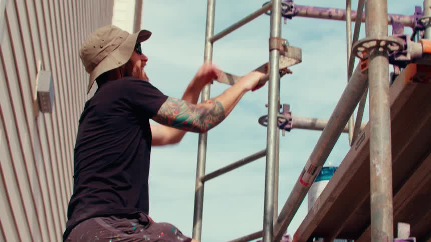 A man carrying some paint up onto scaffolding