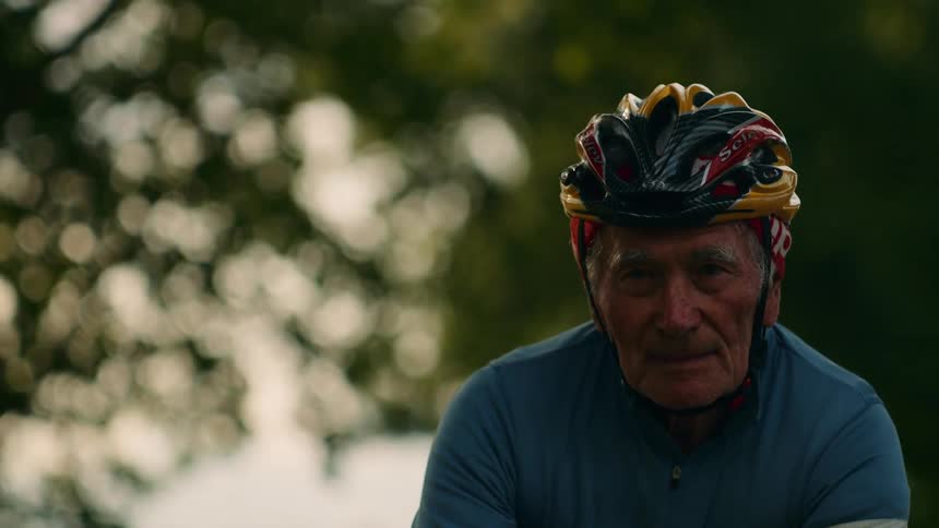 A closeup reveals the weathered and determined face of an older cyclist his focused gaze fixed ahead as he exerts himself on a ride through the countryside