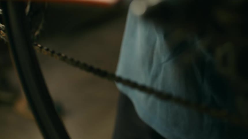 A closeup shot shows a persons hands turning a bicycle chain
