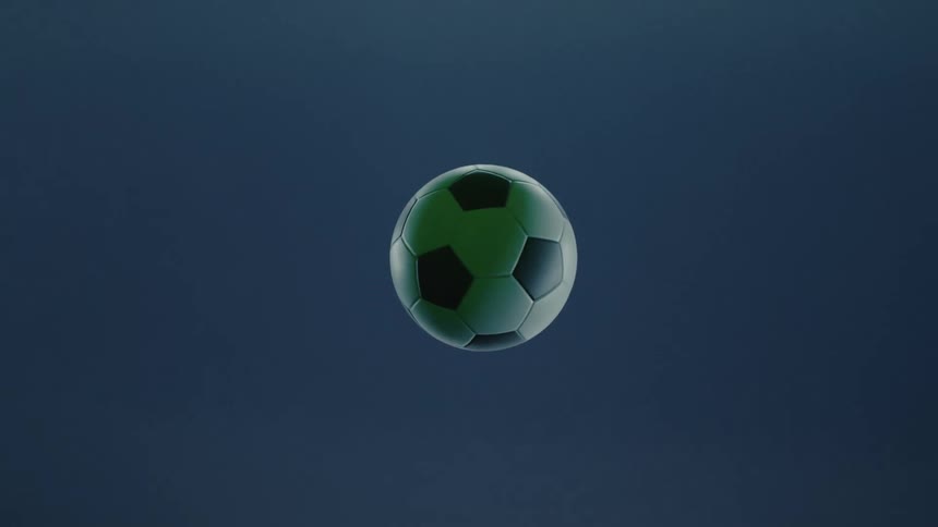 A white and black soccer ball flies through the air on the pitch at night spinning as the stadium lights shine across its surface