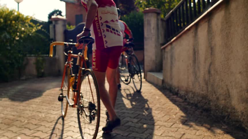 Man walks his bicycle near a building where other cyclists are standing in the street with their bikes