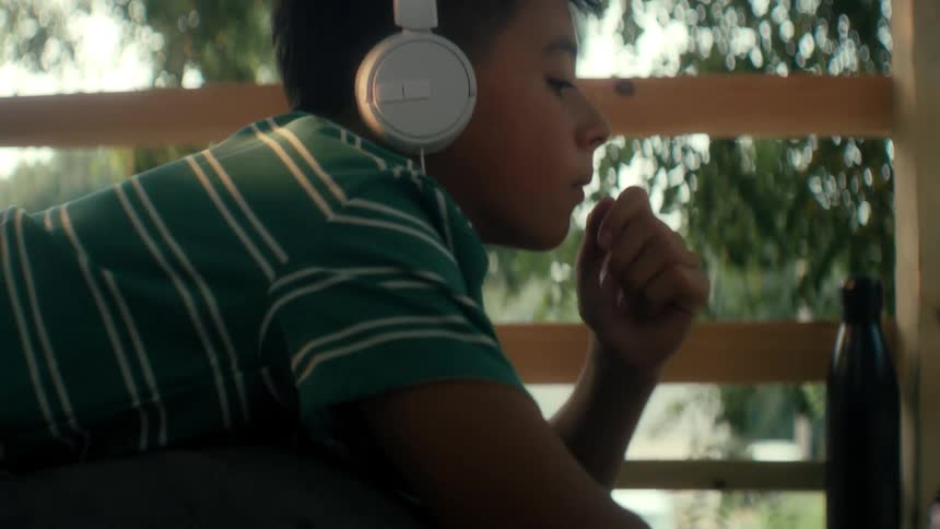 Boy with headphones typing and paying attention while lying in his tree fort in the woods