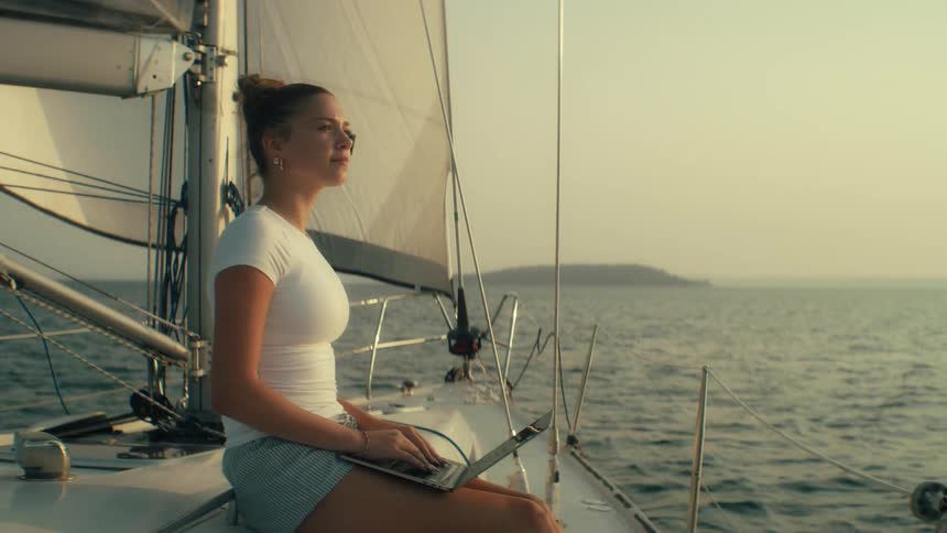 The woman is typing on her laptop while sitting on a sailboat