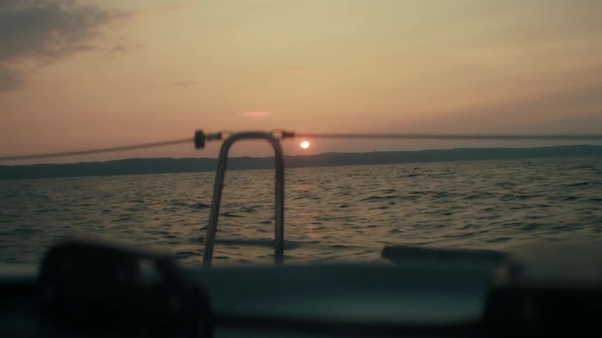 A lowangle shot from a moving boat captures the sun setting over a wide ocean with distant shoreline